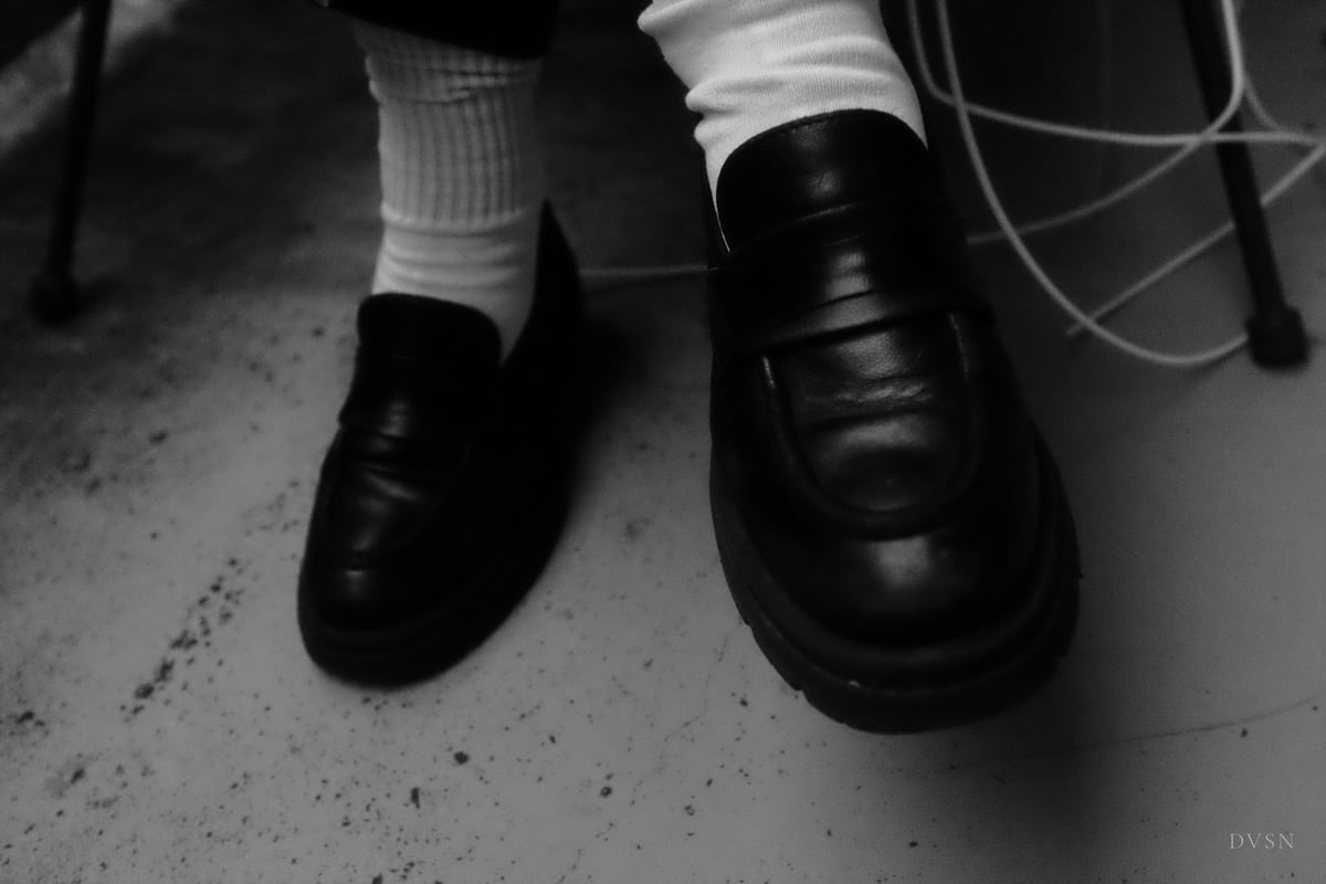 Des mocassins noirs et des chaussettes blanches sur un sol en béton.