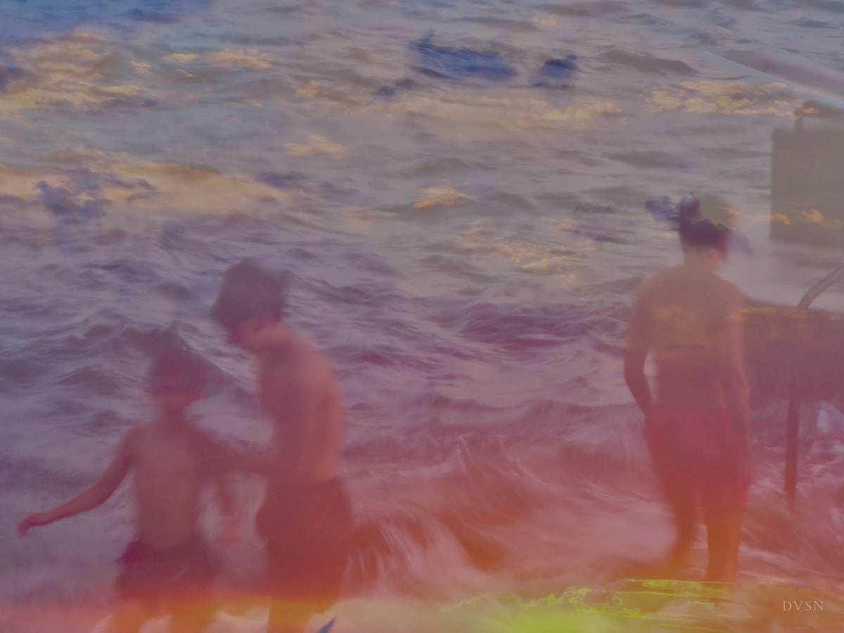 Des baigneurs flous dans les vagues, sous une lumière pastel du soir.