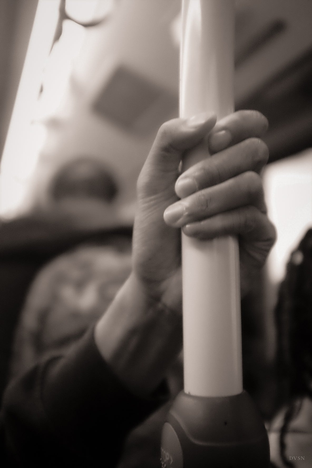 Une main serrant une barre dans un bus, en tons sépia.