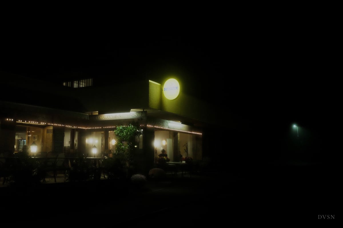 Un restaurant illuminé dans la nuit brumeuse, entouré d'obscurité.