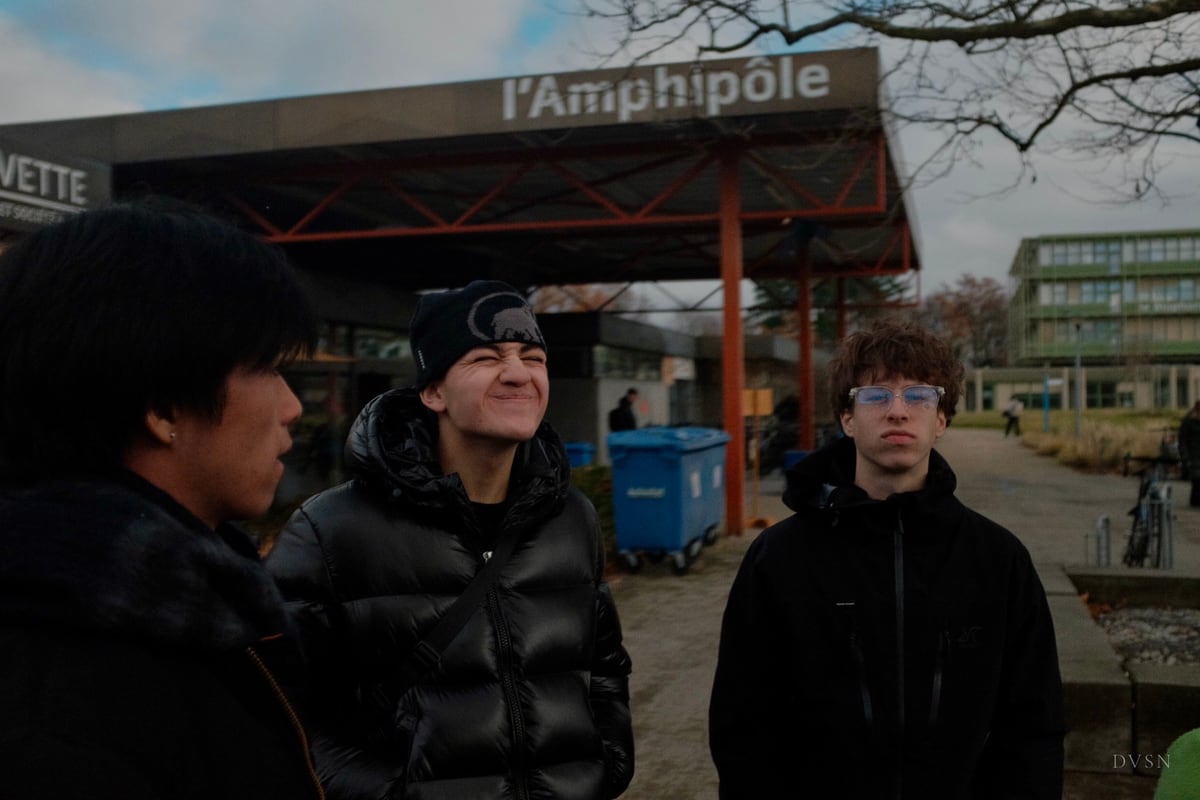 Trois jeunes devant un bâtiment par temps couvert ; l'un plisse les yeux en souriant.