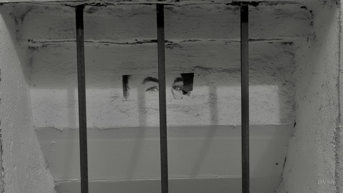 Une paire d'yeux imprimée collée sur un mur, derrière des barreaux.