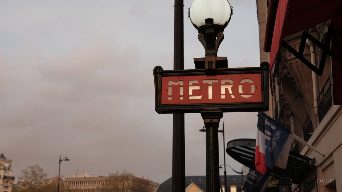 Une enseigne rouge du métro sous un lampadaire à globe, au crépuscule.